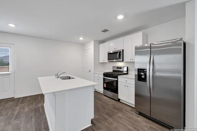 a kitchen with a refrigerator a sink a stove top oven and cabinets