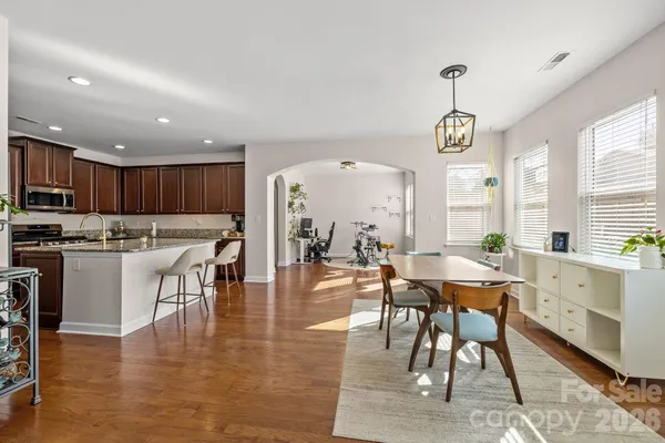 a dining hall with stainless steel appliances granite countertop a stove a refrigerator a kitchen island a dining table and chairs with wooden floor