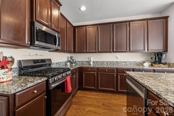 a kitchen with stainless steel appliances granite countertop a stove top oven a sink dishwasher and a microwave oven with wooden cabinets
