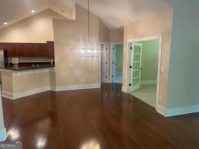 an empty room with wooden floor a flat screen tv and kitchen view