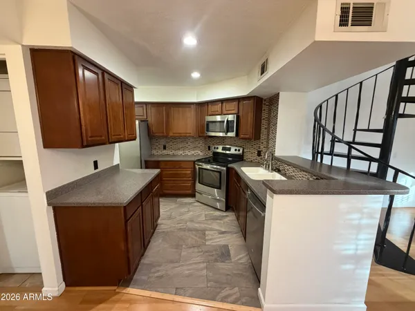 a kitchen with stainless steel appliances granite countertop a stove top oven a sink dishwasher and a refrigerator with wooden floor
