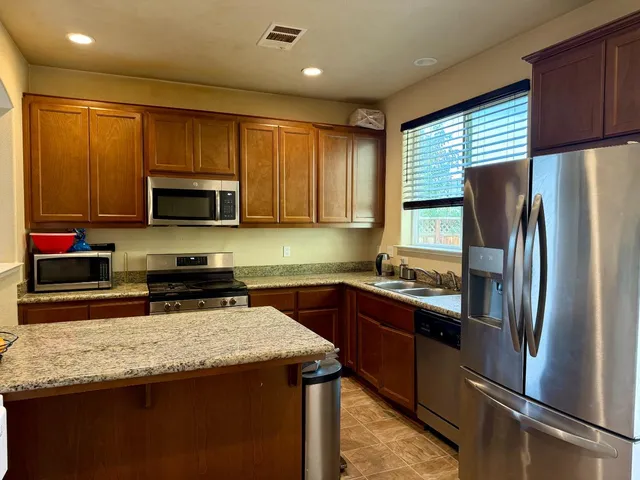 a kitchen with stainless steel appliances granite countertop a refrigerator a sink a stove a microwave and wooden cabinets