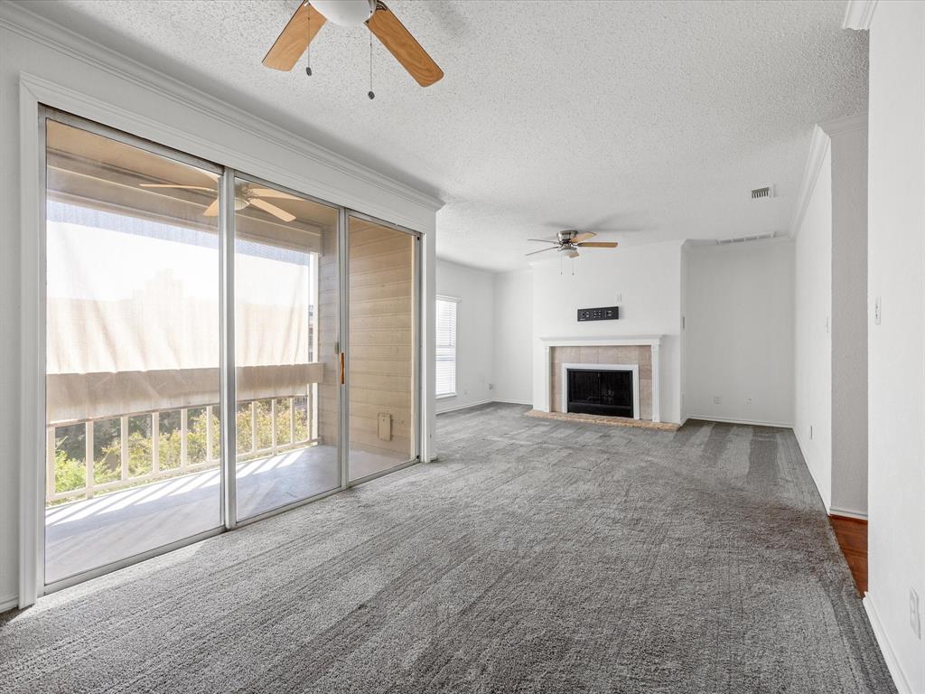 5310 Keller Springs Road, Unit 332 Dallas, TX 75248 - Photo 4 of 39 Unfurnished living room featuring a textured ceiling, a tile fireplace, carpet, and ornamental molding