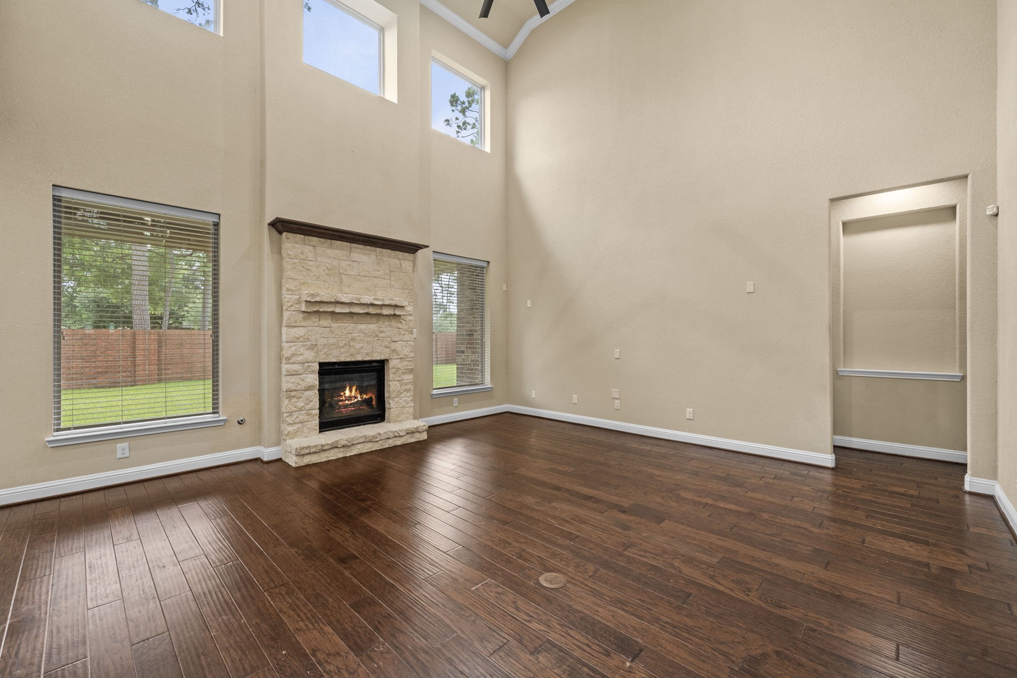 14215 Spindle Arbor Road Cypress, TX 77429 - Photo 11 of 47 This spacious living room features high ceilings, large windows for natural light, a cozy stone fireplace, and elegant hardwood floors, creating a warm and inviting atmosphere.