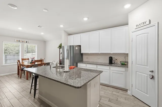 a kitchen with stainless steel appliances granite countertop a dining table chairs and white cabinets