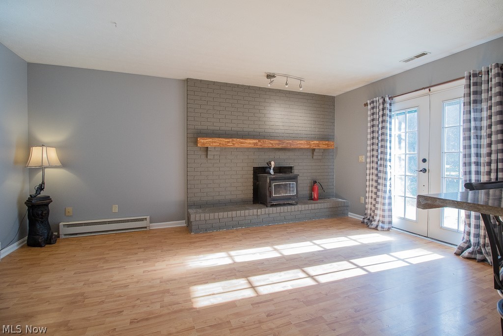 2744 Haines Road Madison, OH 44057 - Photo 11 of 26 Family room with a wood stove, french doors, wood-style floors, rail lighting, and a baseboard heating unit