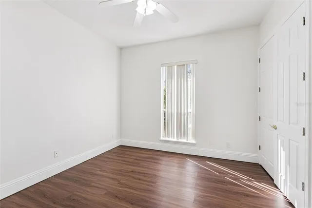 an empty room with wooden floor chandelier fan and windows