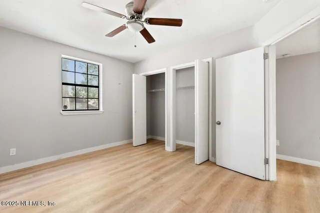 a view of an empty room with wooden floor and a ceiling fan