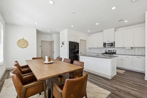 a kitchen with stainless steel appliances granite countertop a stove a sink a refrigerator and white cabinets with wooden floor