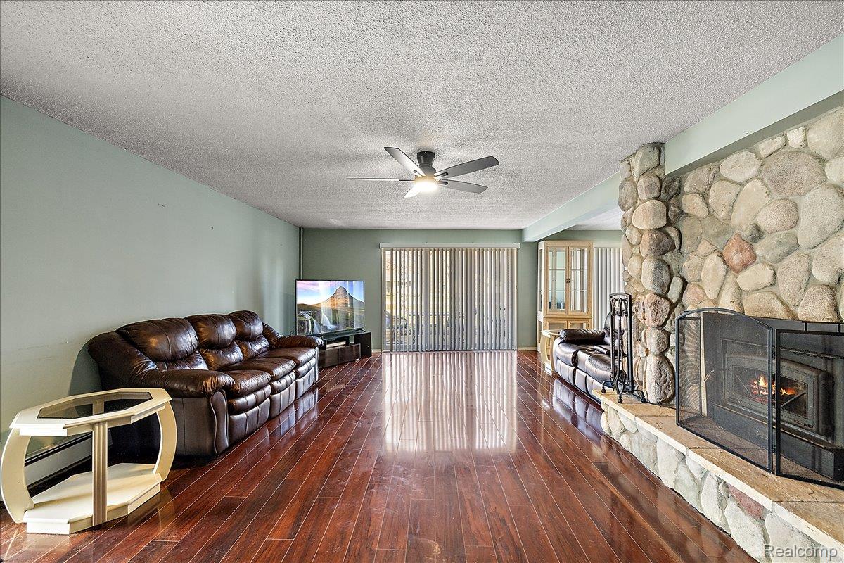 4705 Ketchum Road St. Clair, MI 48079 - Photo 13 of 58 Living room featuring dark wood finished floors, a stone fireplace, a textured ceiling, and a ceiling fan