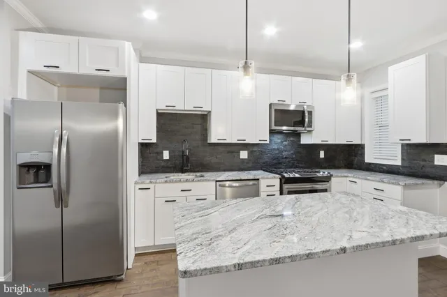 a kitchen with stainless steel appliances kitchen island granite countertop a refrigerator a sink a stove and white cabinets with wooden floor