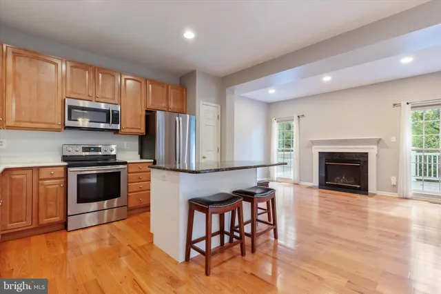 a kitchen with granite countertop a stove top oven a sink dishwasher a refrigerator and a fireplace with wooden floor