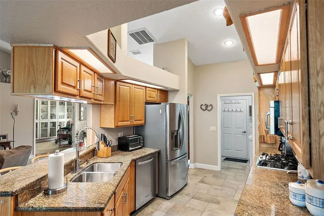 a kitchen with stainless steel appliances granite countertop a refrigerator a stove and a sink with wooden cabinets