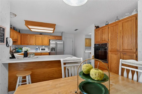 a living room with stainless steel appliances furniture a rug kitchen view and a table