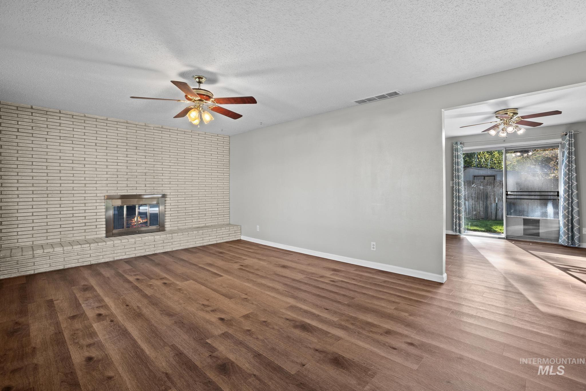 Wood-finish flooring, brick fireplace with hearth, stainless steel fireplace insert, and ceiling fans