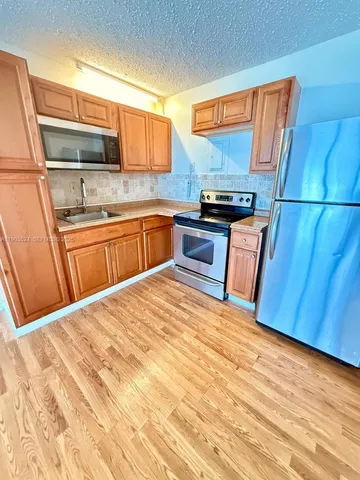 a kitchen with stainless steel appliances kitchen island granite countertop wooden cabinets a stove top oven a sink and dishwasher