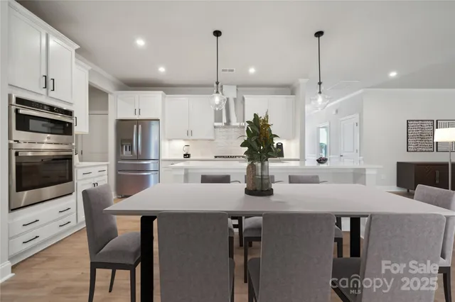 a kitchen with stainless steel appliances granite countertop a sink a stove a refrigerator and a dining table with wooden floor