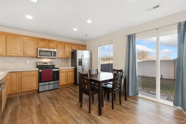 a kitchen with stainless steel appliances granite countertop a stove a refrigerator a sink a dining table and chairs with wooden floor