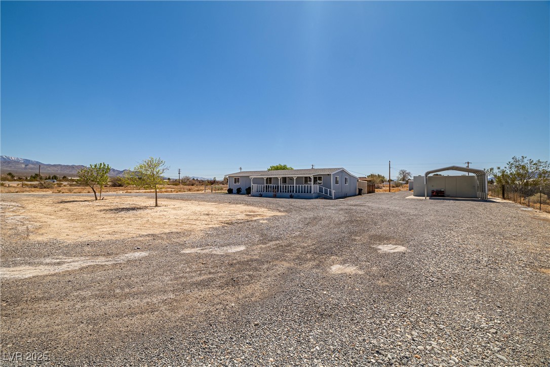 101 West Pechstein Road Pahrump, NV 89060 - Photo 2 of 33 View of yard featuring covered porch, 4 outbuilding's, gravel horseshoe driveway, a carport, and mountain views.