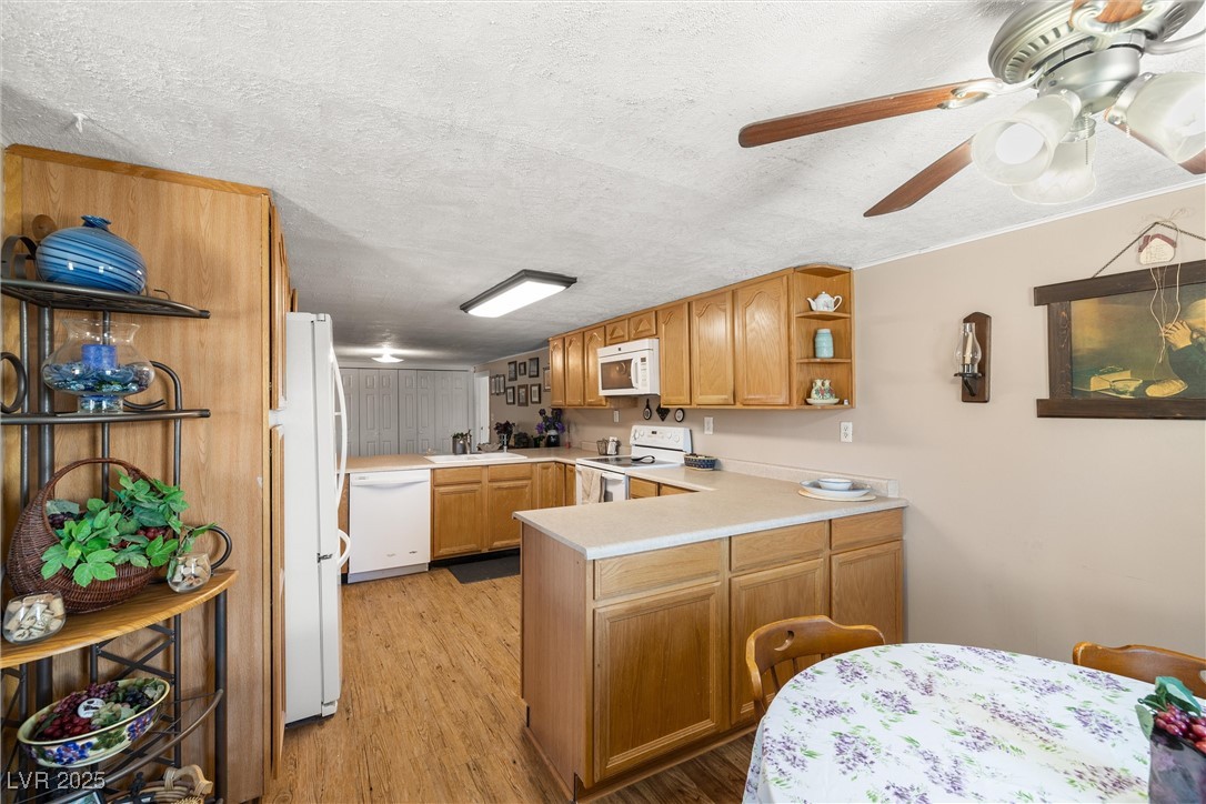 101 West Pechstein Road Pahrump, NV 89060 - Photo 9 of 33 Kitchen featuring custom cabinets, light wood-type flooring, white appliances, ceiling fan, and a peninsula breakfast bar area.
