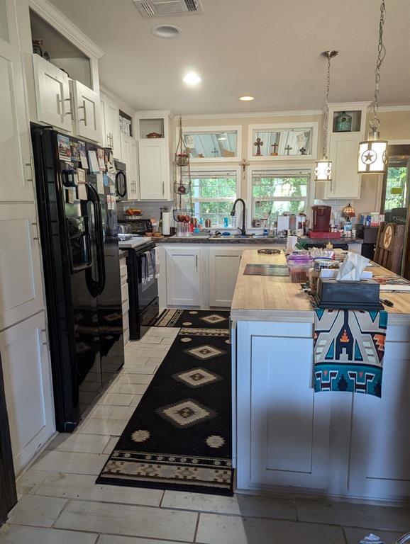 Kitchen with black appliances, wood counters, backsplash, sink, and white cabinets