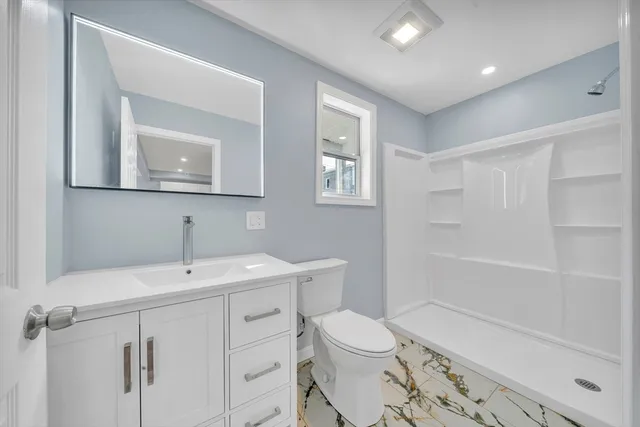 a bathroom with a toilet a sink a mirror a shower a vanity and window