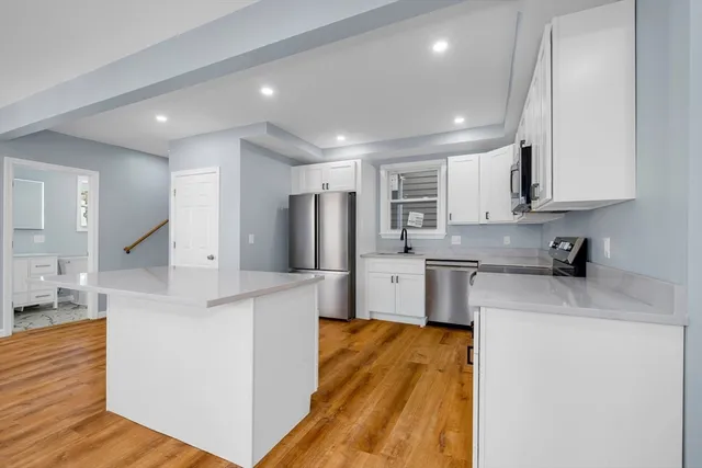 a kitchen with stainless steel appliances granite countertop a sink dishwasher a refrigerator and white cabinets with wooden floor