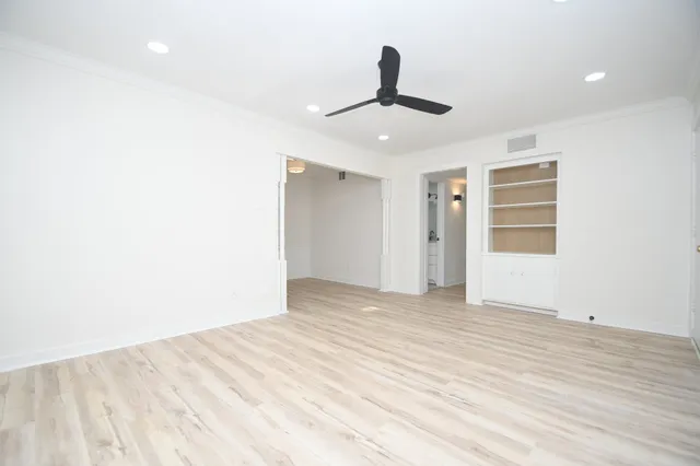 a view of an empty room with chandelier fan and wooden floor
