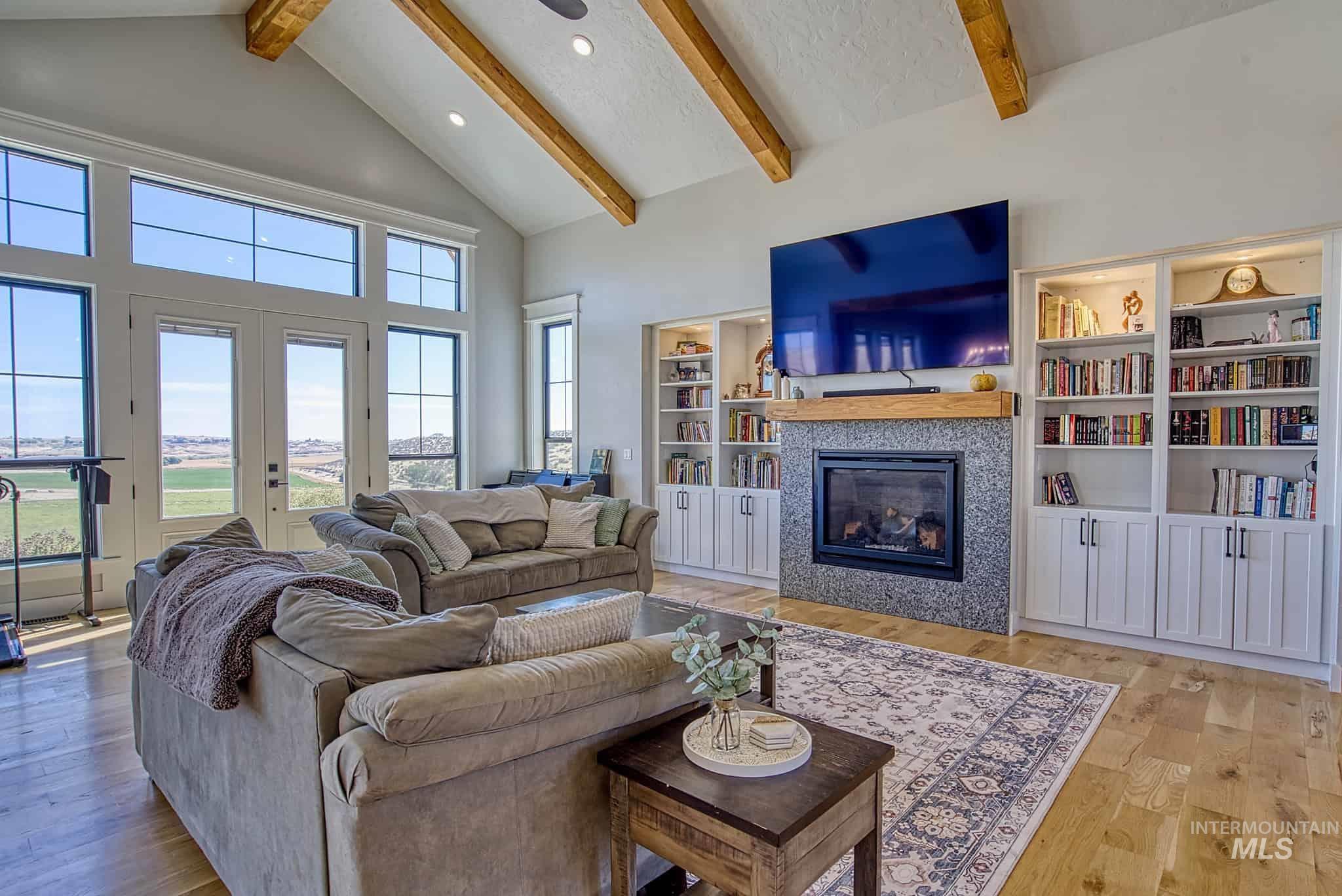 876 Coyote Gulch Road Adrian, OR 97901 - Photo 25 of 50 Vaulted ceiling with exposed wood beams, wood-finish flooring, built-in shelving, stone-finish fireplace surround, and multiple windows with clear glass panes