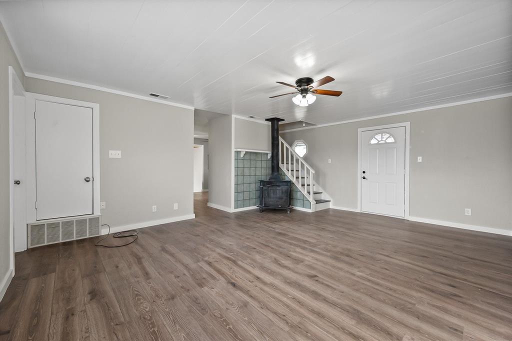 443 County Road 3799 Springtown, TX 76082 - Photo 14 of 33 Unfurnished living room with a wood stove, stairs, ornamental molding, wood finished floors, and a ceiling fan