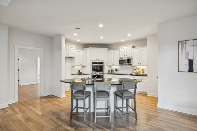 a kitchen with stainless steel appliances granite countertop white cabinets a sink a stove a refrigerator and microwave with wooden floor