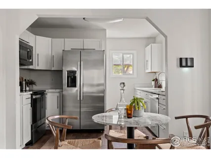 a kitchen with stainless steel appliances kitchen island granite countertop a refrigerator a stove a sink and white cabinets with wooden floor