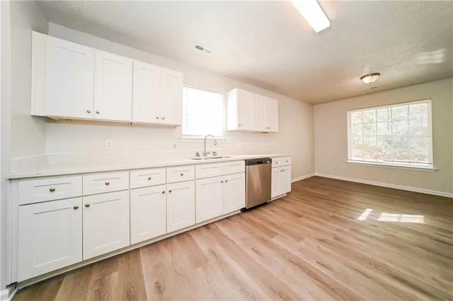 a large white kitchen with granite countertop a stove a sink white cabinets and wooden floor next to a window