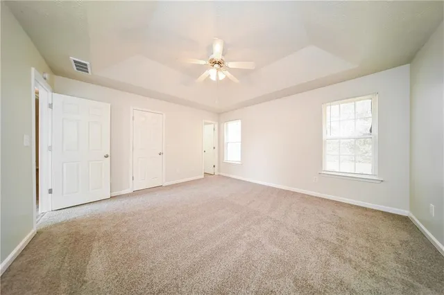 an empty room with chandelier fan and windows