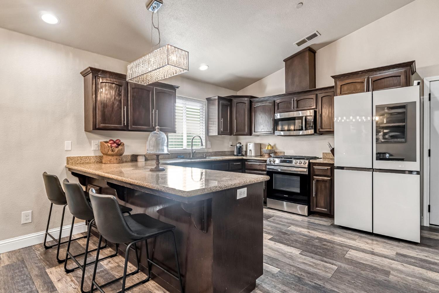25802 El Monte Way Madera, CA 93638 - Photo 12 of 39 kitchen featuring a kitchen bar, dark wood finish cabinetry, a peninsula, stainless steel appliances, and dark stone countertops
