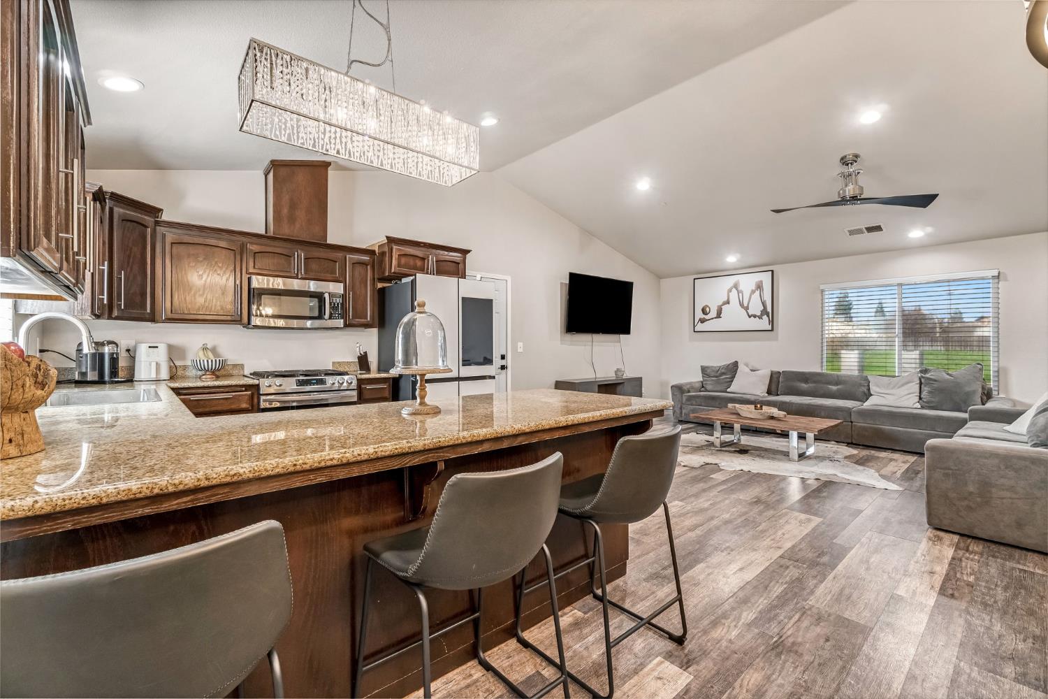 25802 El Monte Way Madera, CA 93638 - Photo 13 of 39 kitchen featuring light stone countertops, dark wood finish cabinetry, a peninsula, healthy amount of natural light, and lofted ceiling