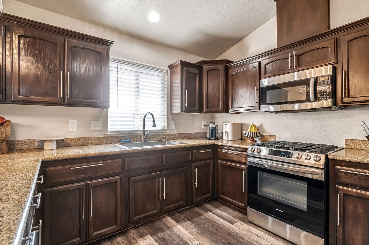 25802 El Monte Way Madera, CA 93638 - Photo 15 of 39 kitchen with dark wood finish cabinets, stainless steel appliances, light stone counters, and lofted ceiling