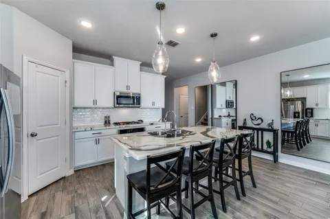 a kitchen with stainless steel appliances granite countertop a stove a refrigerator a sink dishwasher a dining table and chairs with wooden floor