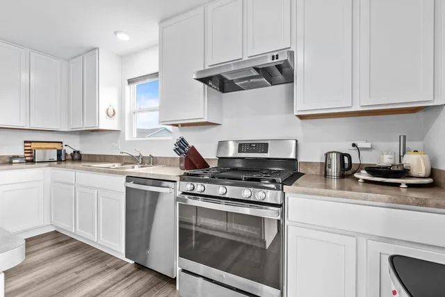 a kitchen with a refrigerator a sink dishwasher a stove and white cabinets with wooden floor