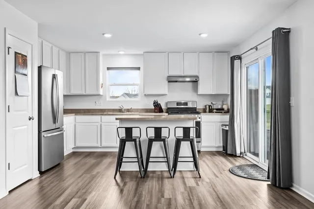 a kitchen with stainless steel appliances a refrigerator a stove a sink dishwasher and white cabinets with wooden floor