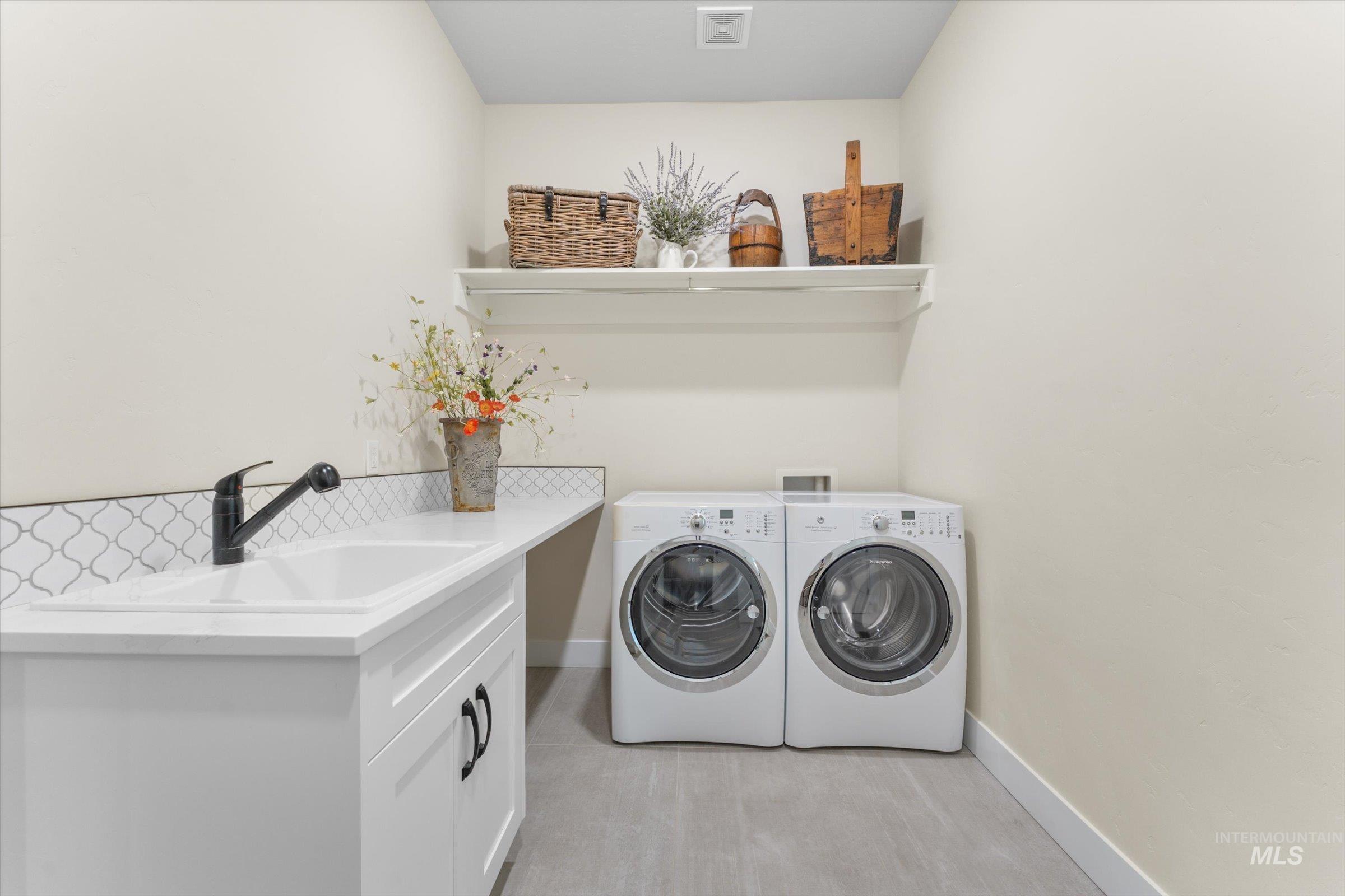 6585 South Pemberley Way Meridian, ID 83642 - Photo 36 of 43 Laundry area featuring a built-in sink with a matte black faucet, white cabinetry, decorative arabesque tile backsplash, and a wall-mounted shelf