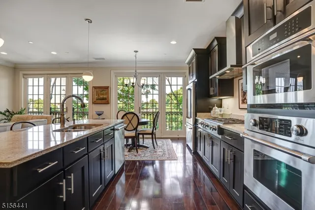 a kitchen with stainless steel appliances granite countertop a stove top oven a sink dishwasher a dining table and chairs with wooden floor