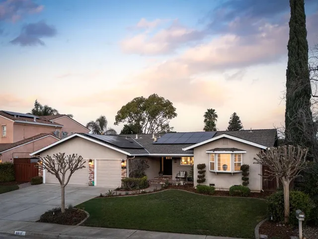 a view of a white house next to a yard with big trees