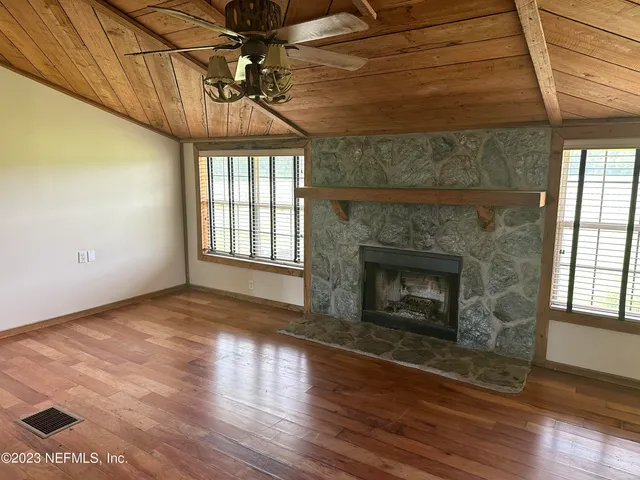 a view of an empty room with wooden floor fireplace and a window