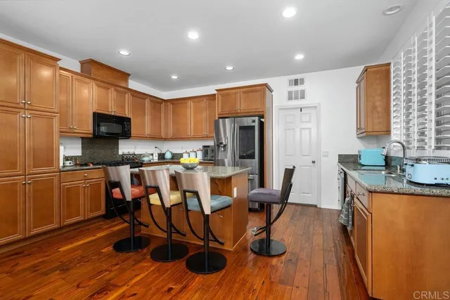 a kitchen with stainless steel appliances granite countertop a refrigerator a stove top oven a sink dishwasher and white cabinets with wooden floor