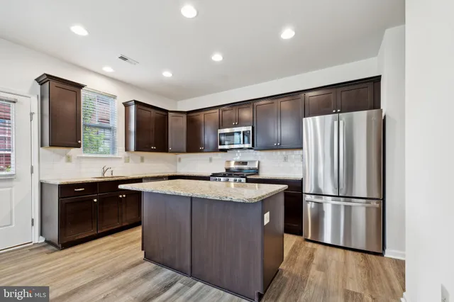 a kitchen with stainless steel appliances granite countertop a refrigerator a sink dishwasher a oven with wooden cabinets and wooden floor