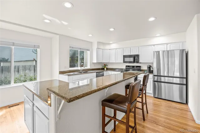 a kitchen with stainless steel appliances granite countertop a refrigerator a stove a sink a dining table and chairs