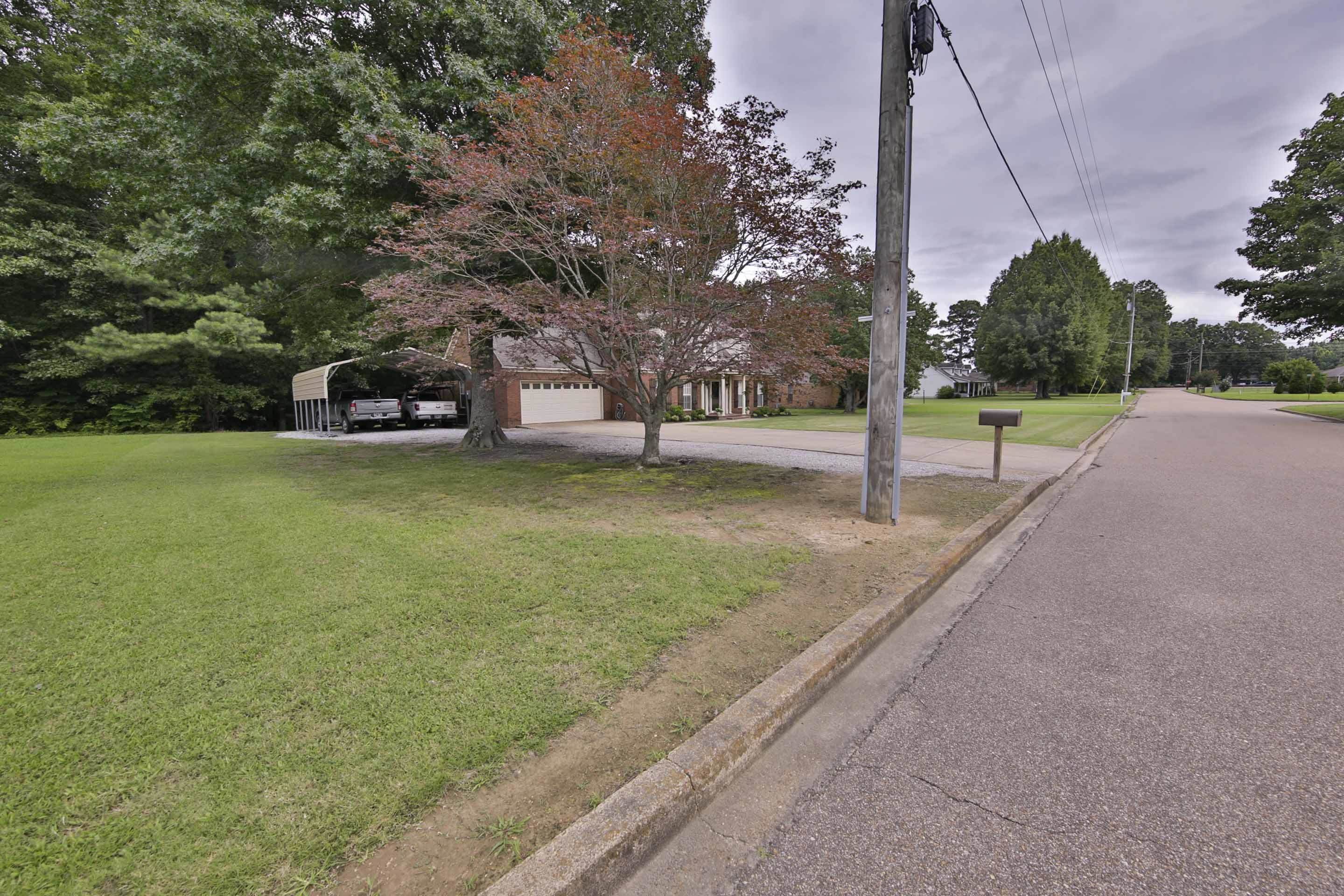 104 Miller Road Covington, TN 38019 - Photo 4 of 25 Brick exterior residence with an attached two-car garage, mature trees, a metal carport, and a grassy front lawn