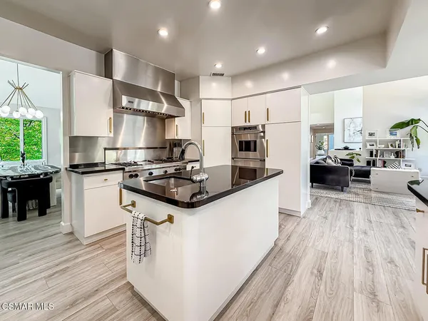 a kitchen with stainless steel appliances kitchen island granite countertop a stove a sink dishwasher a refrigerator and white cabinets with wooden floor