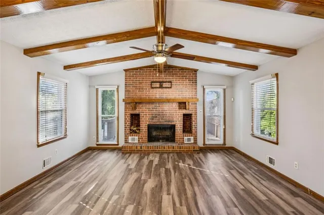 a view of an empty room with wooden floor fireplace and a window